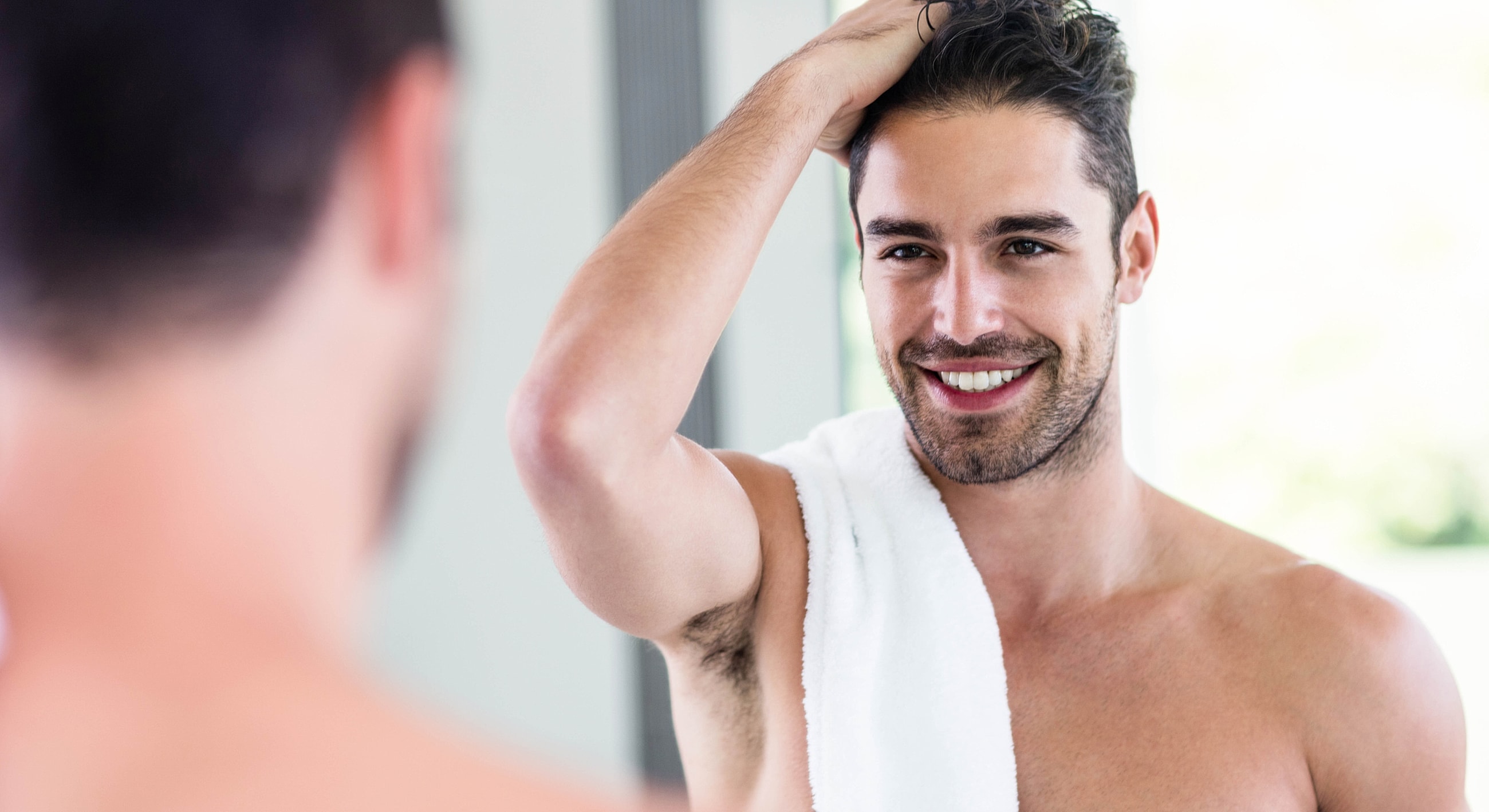 Man with towel smiling at mirror.